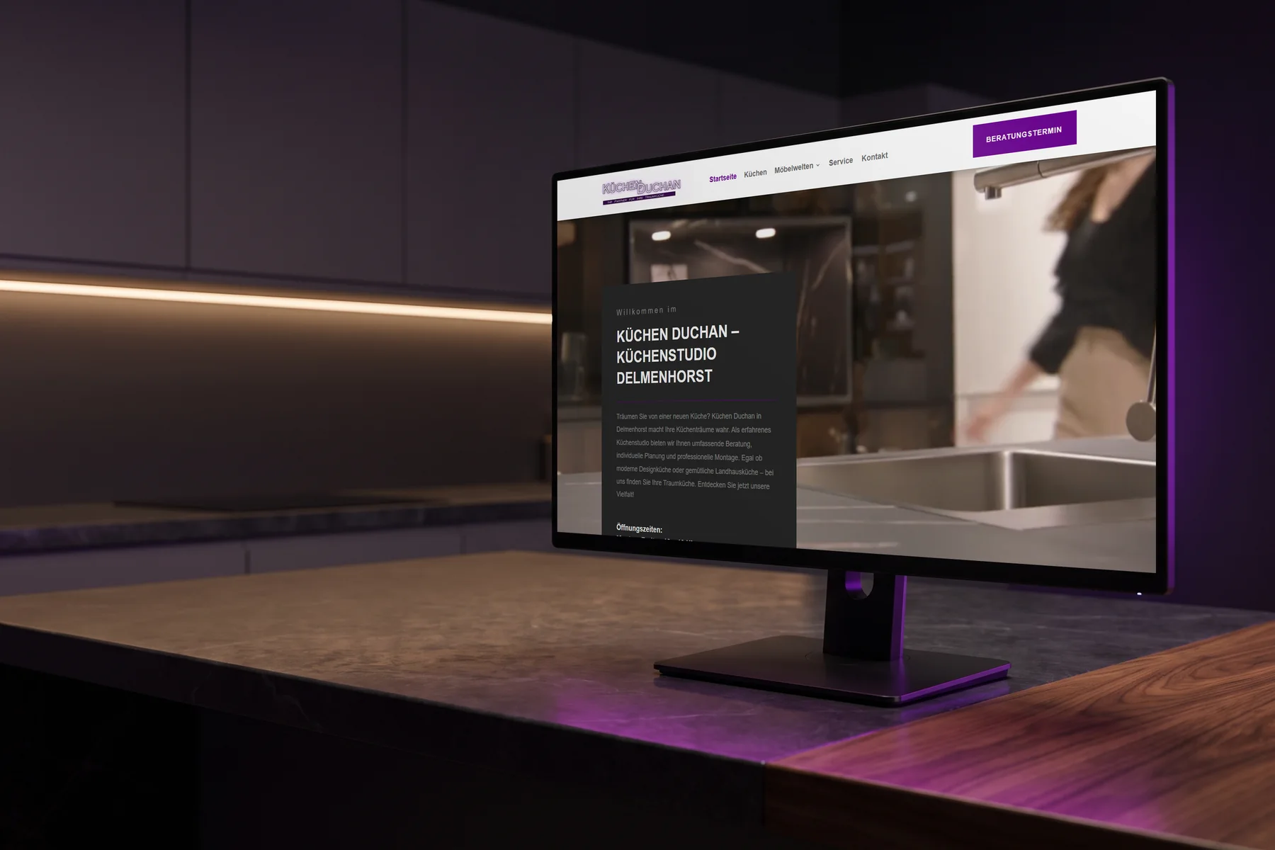 Monitor auf einer Arbeitsplatte aus Stein und Holz zeigt die Website eines Küchenstudios als Referenz.