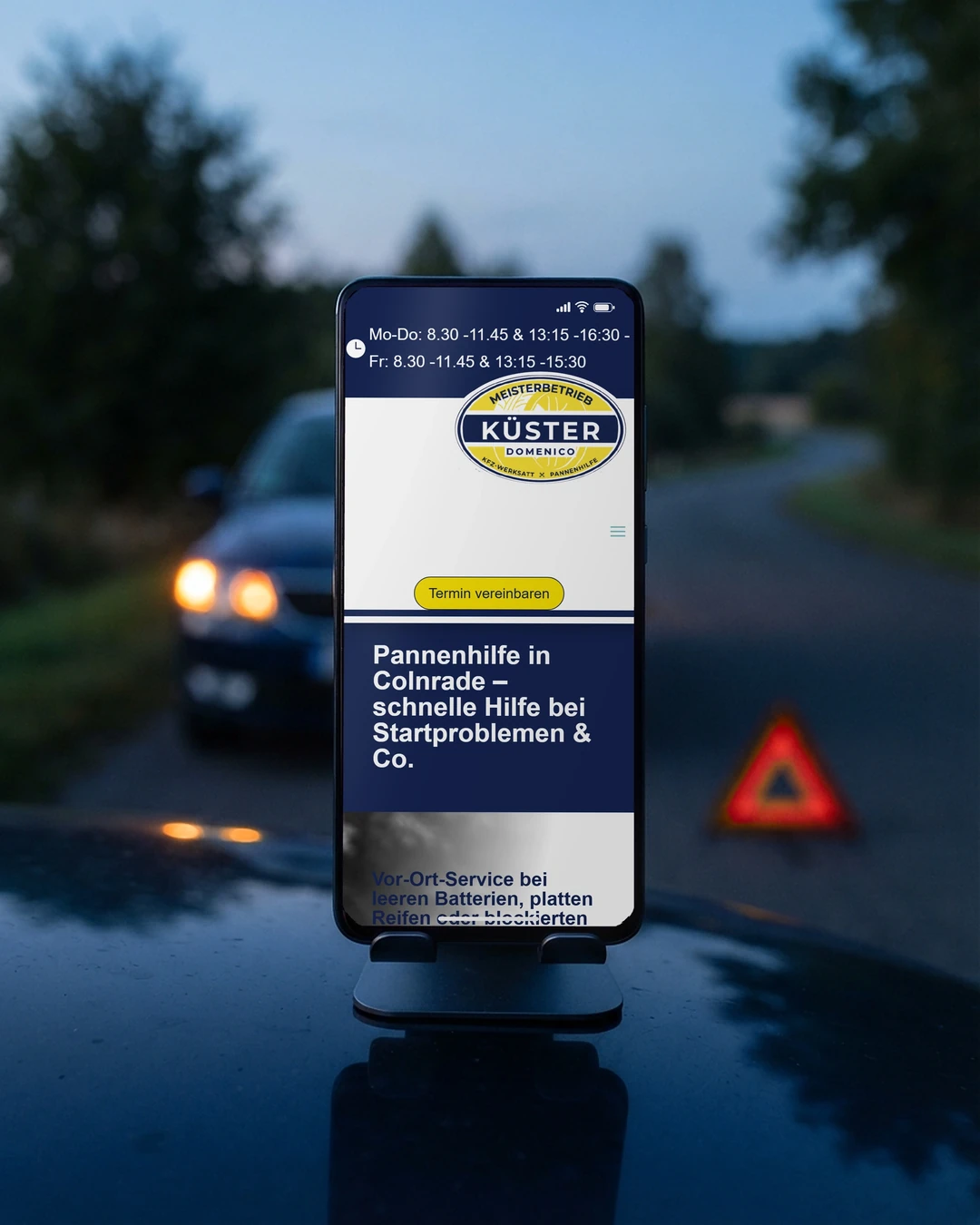 Pannenhilfe-Seite der Autowerkstatt Küster am Handy auf der Motorhaube: Webseite für Kfz-Betriebe trennt Termin und Panne