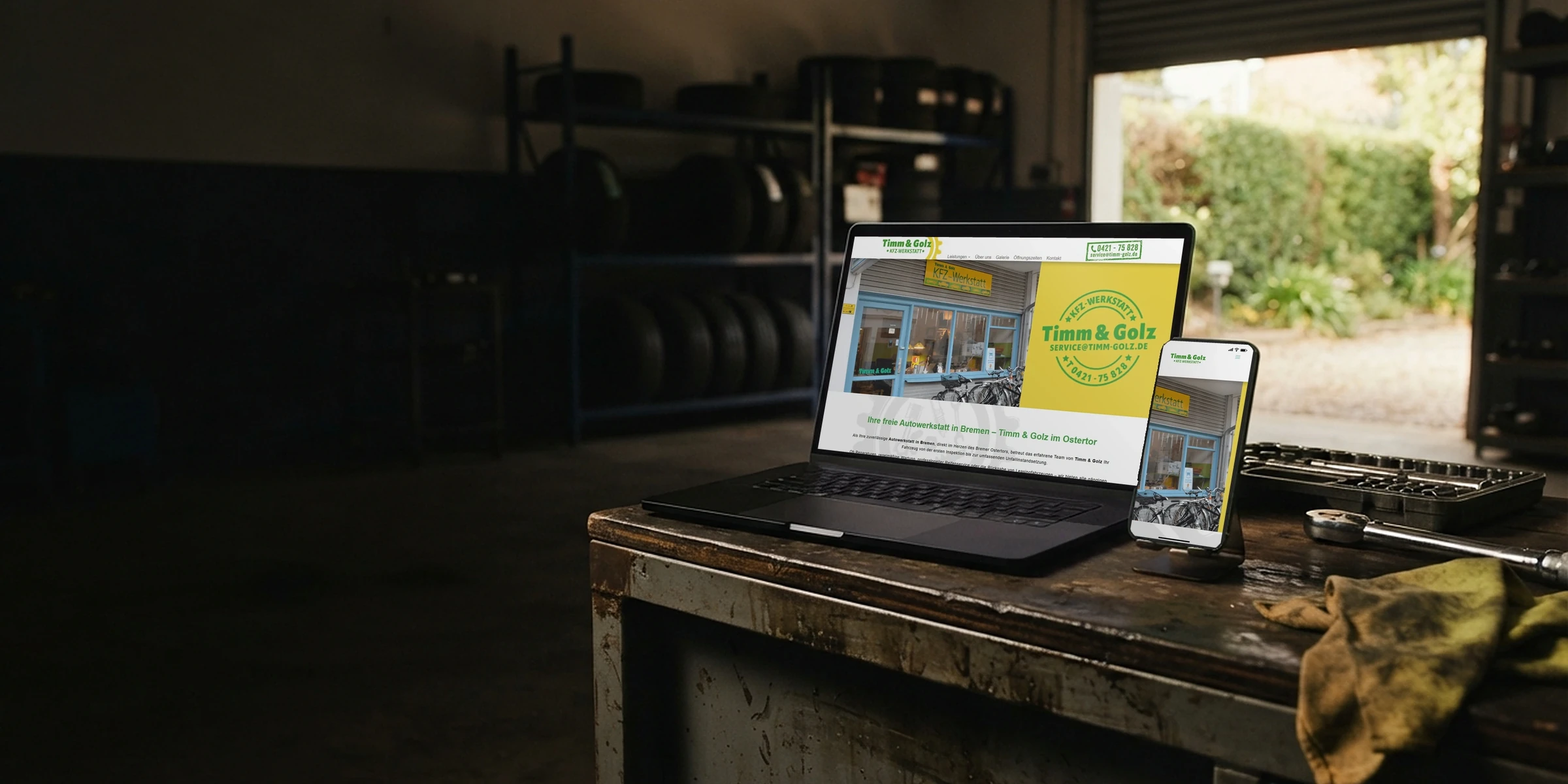 Webseite von Timm & Golz auf Laptop und Handy am offenen Werkstatttor: Webdesign für die Kfz-Werkstatt